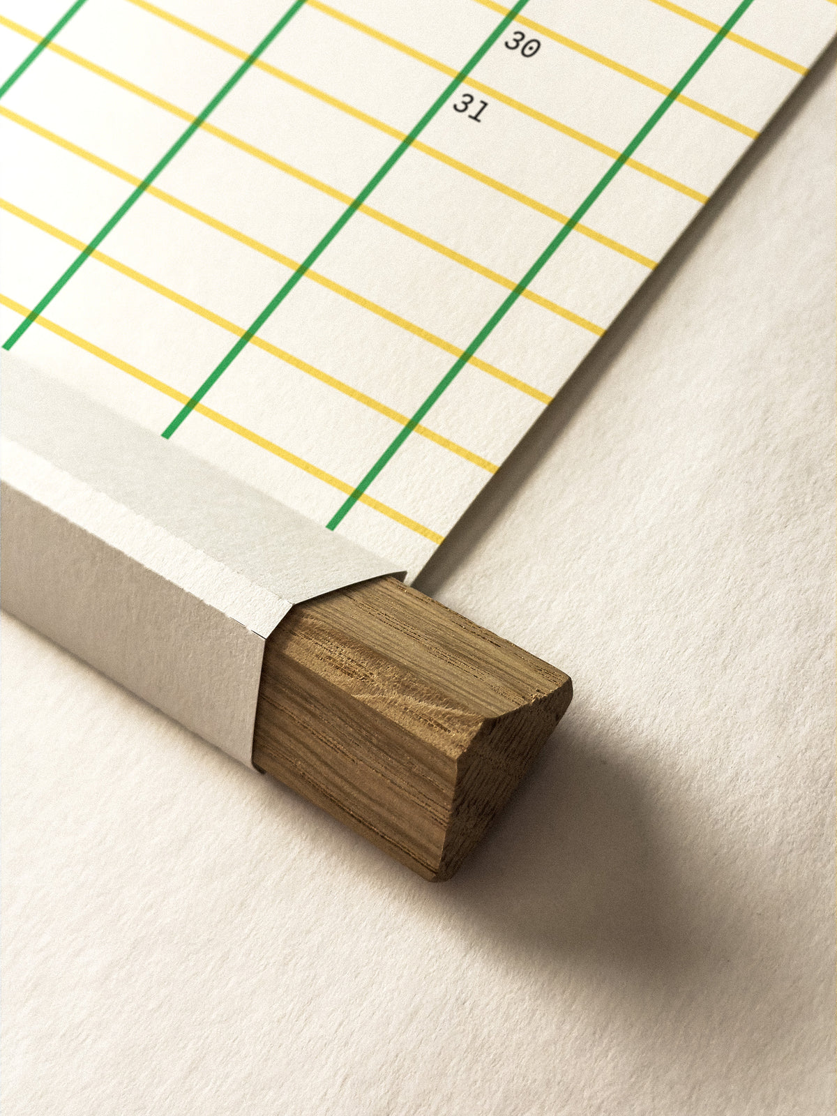 A close-up of a wall planner page with a wooden hanger frame, showing printed green and yellow grid lines and the numbers 30 and 31 on a light neutral background.