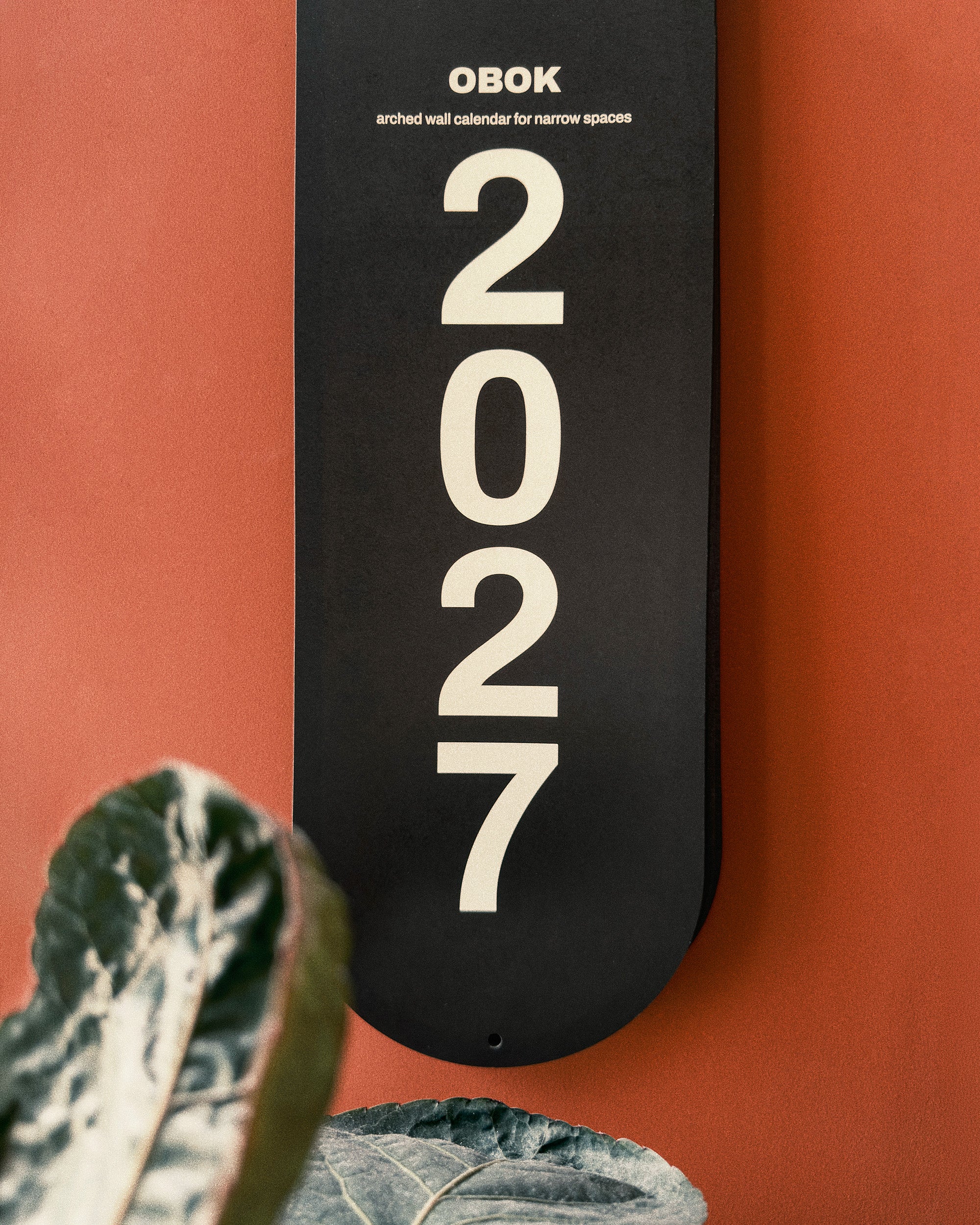 Black arch-shaped wall calendar with '2027' on a red background, featuring the name 'OBOK'.