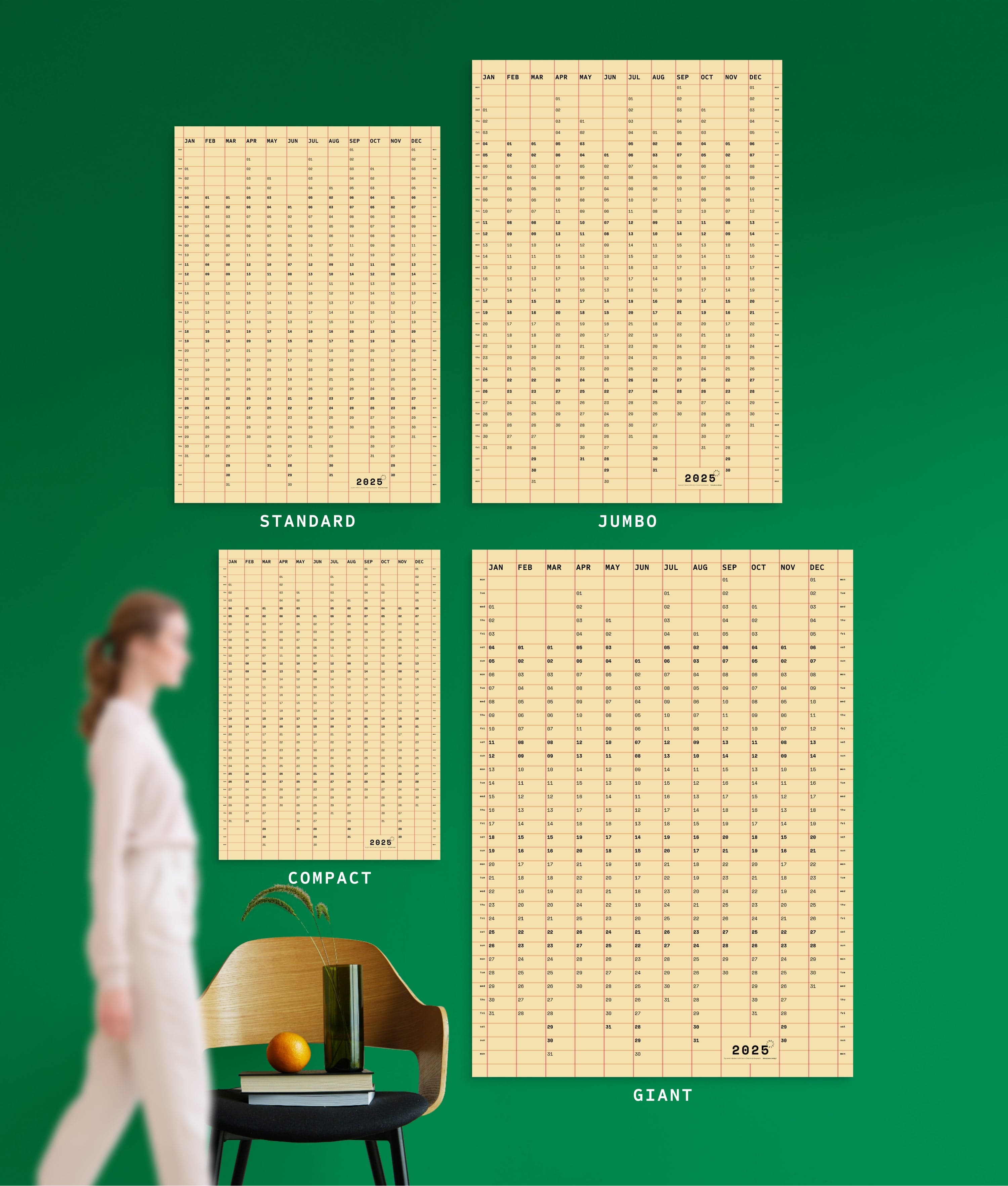 4 sizes of Squared in Cream-pink yearly planner on green wall, with person, chair, orange and vase shown for scale