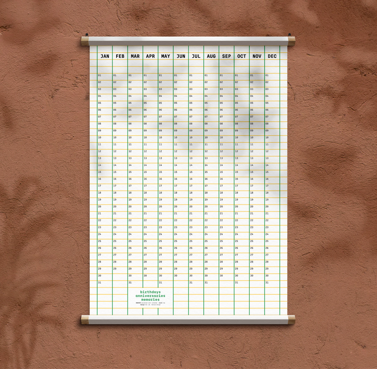 A vertical hanging calendar poster with a grid of dates and months labelled JAN through DEC, mounted against a textured brown wall.