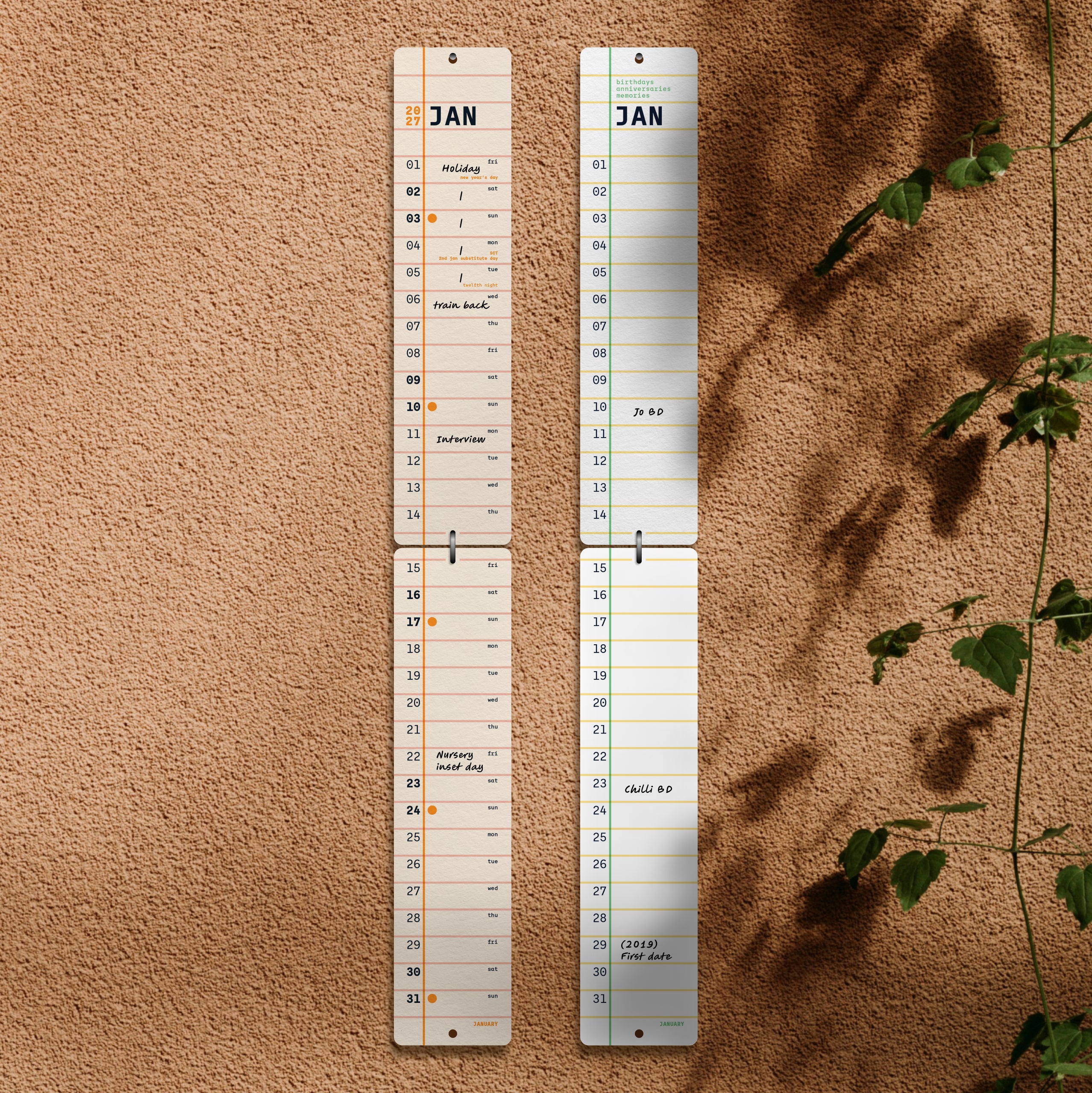 Two calendars on a rendered wall with plant leaves to the side.